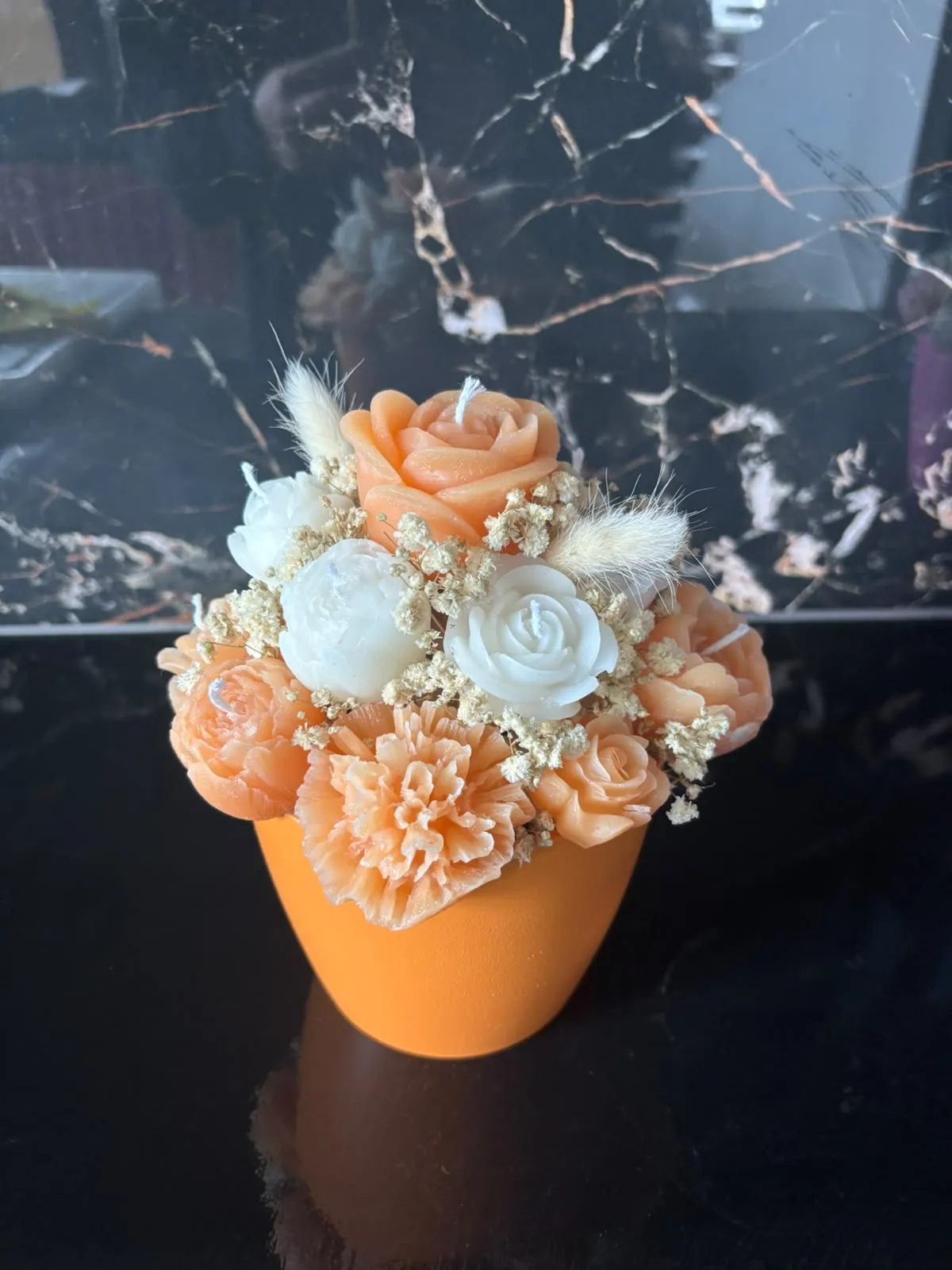 Bouquet de velas em forma de rosas e cravos laranja, pêssego e brancos, com gipsófila e espigas secas, num vaso laranja