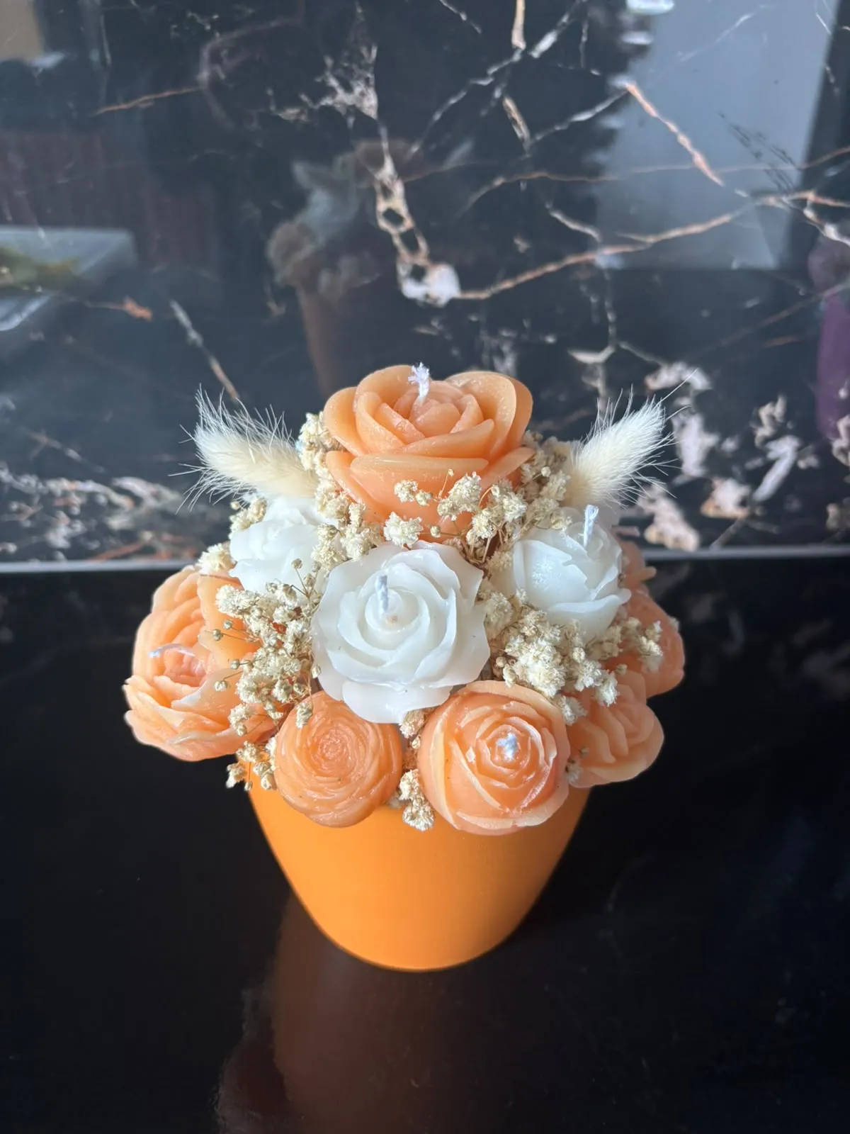 Bouquet de velas em forma de rosas e cravos laranja, pêssego e brancos, com gipsófila e espigas secas, num vaso laranja