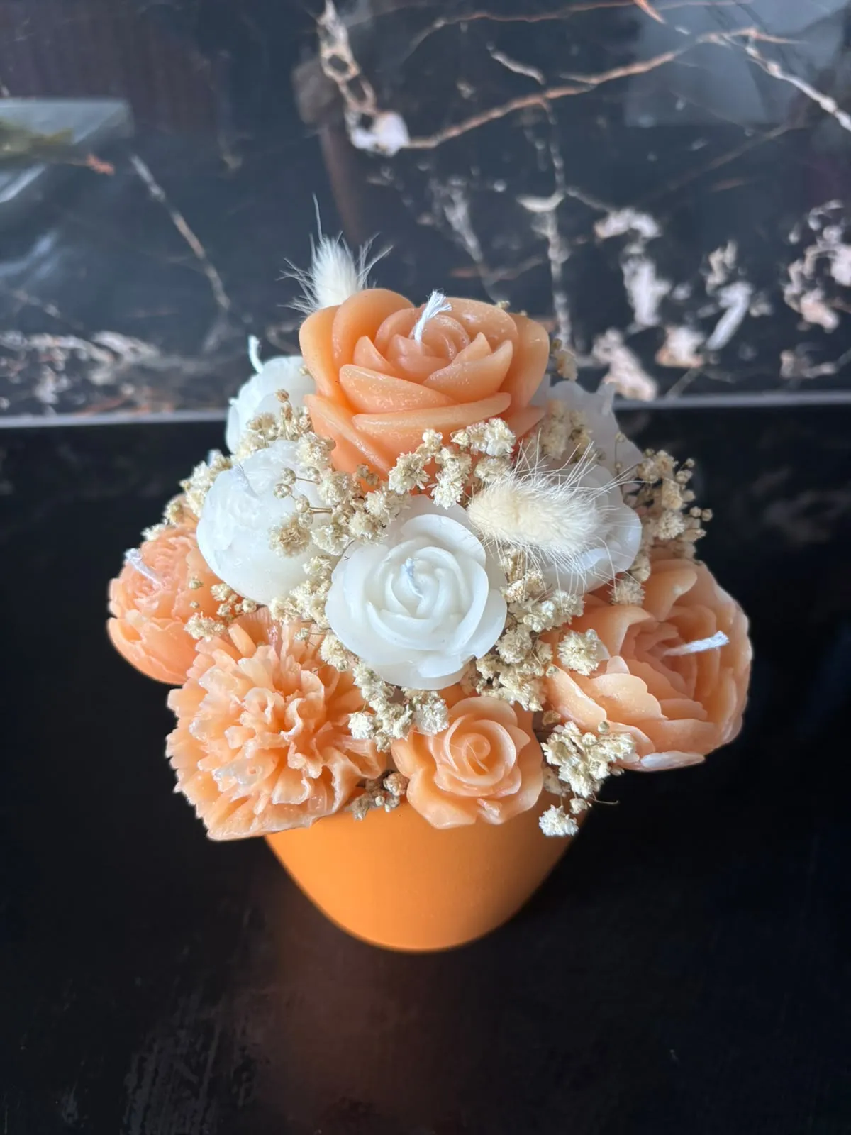 Bouquet de velas em forma de rosas e cravos laranja, pêssego e brancos, com gipsófila e espigas secas, num vaso laranja