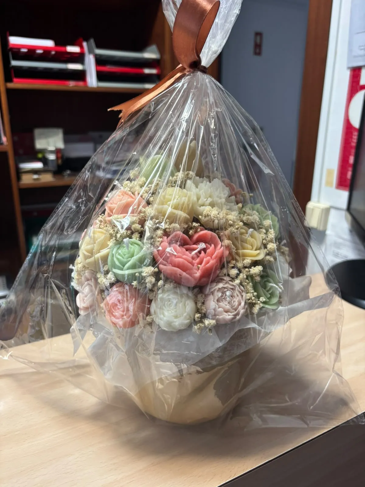 Bouquet de velas em tons pastel de rosa, verde e creme, embrulhado em celofane com laço castanho